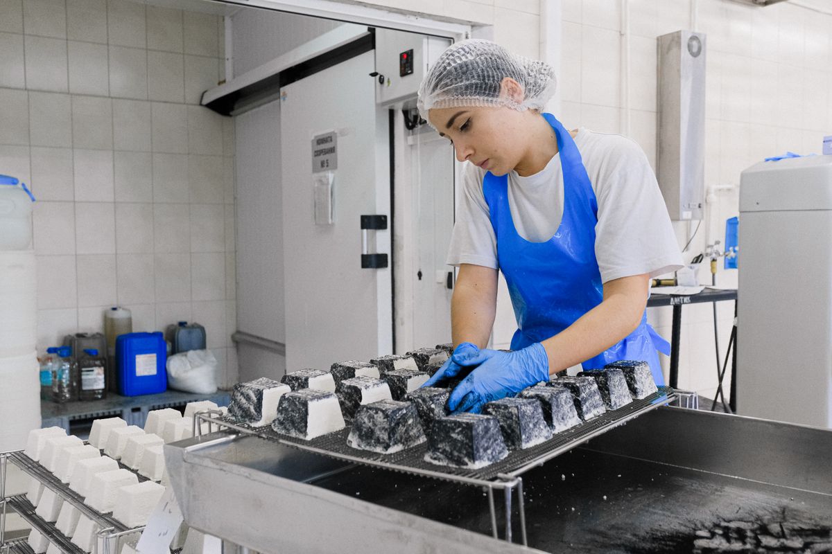 Operario con gorro y guantes revisando producto en bandejas dentro de una planta de alimentos